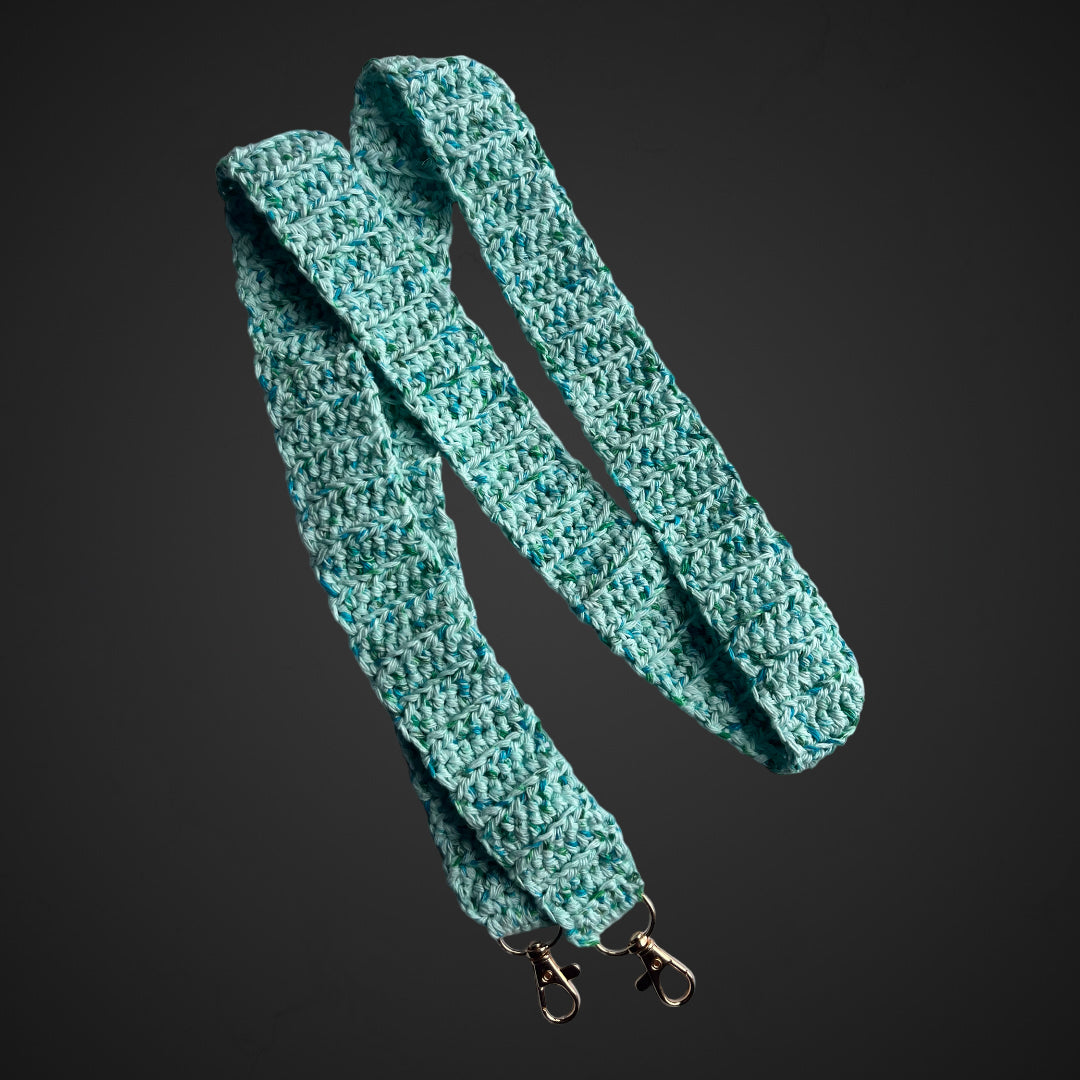 Crocheted phone safety tether in an aquamarine colour with variegations of blue and green.  The tether has two lobster clasps attached at either end in antique gold. 